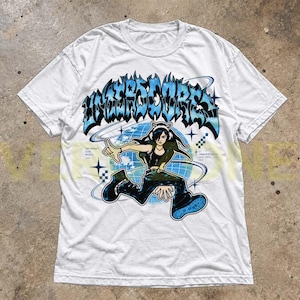 May include: A white short-sleeve t-shirt featuring a graphic print of a character wearing cat-ear headphones in front of a blue globe. The text "UNDERSCORES" appears in a stylized blue font above the character, with additional small text details.
