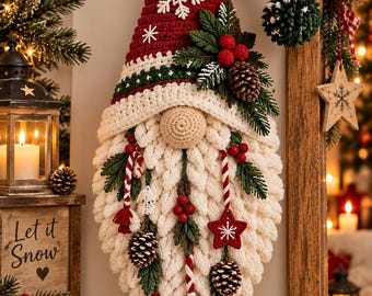 May include: A hanging crochet gnome decoration featuring a tall red hat with white snowflake accents and a dark green pom-pom. The gnome has a beige round nose, a thick white textured beard, and is adorned with pinecones, red berries, and stars.