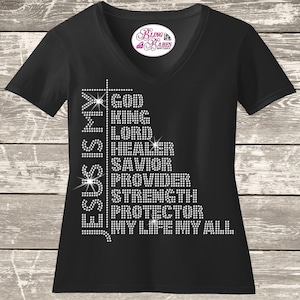 A black t-shirt with white text and rhinestones on it, displayed on a wooden background.