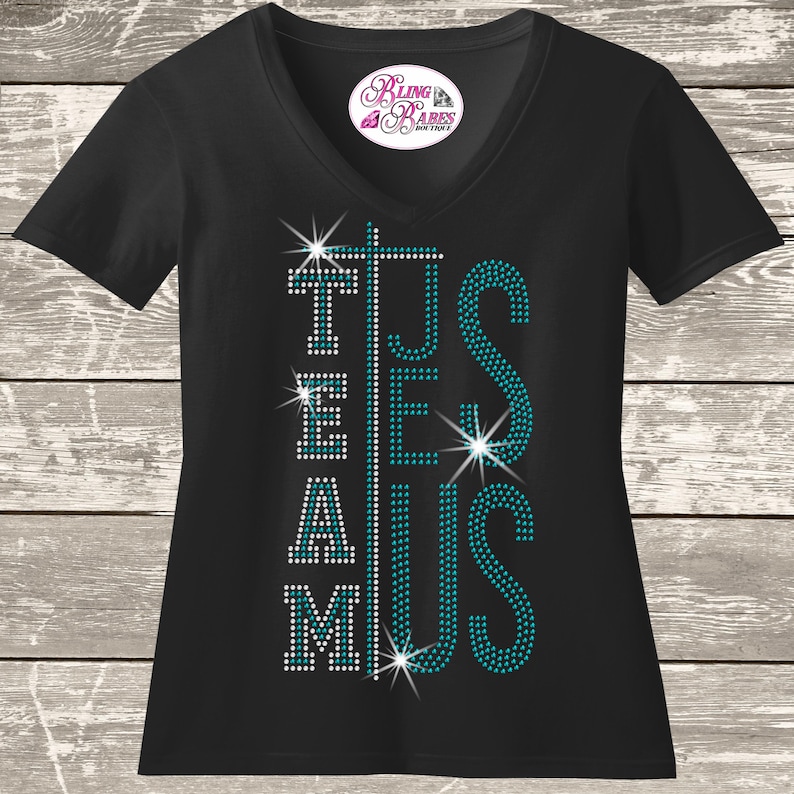 A black t-shirt with teal and white rhinestones on it, featuring the text "TEAM JESUS" in a stylized font.