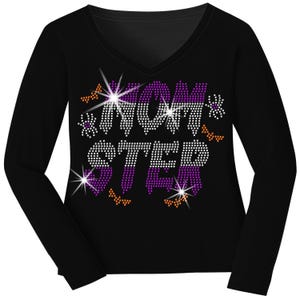 May include: A black long-sleeve V-neck shirt featuring a rhinestone graphic that reads MONSTER. The letters are filled with purple, white, and black rhinestones, accented by small orange bats and purple spiders surrounding the text design.