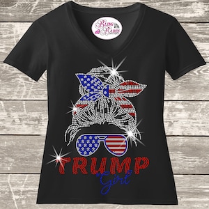 A black t-shirt with a graphic design featuring a stylized female figure wearing sunglasses and a patriotic American flag pattern. The text "Trump girl" is displayed below the figure.