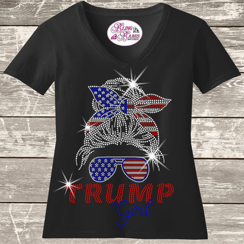 A black t-shirt with a graphic design featuring a stylized female figure wearing sunglasses and a patriotic American flag pattern. The text "Trump girl" is displayed below the figure.