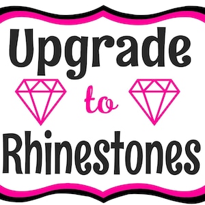 May include: A white sign with a black and pink border features the words "Upgrade to Rhinestones" in black lettering. Two pink diamond shapes flank the word "to". The sign is a decorative element.