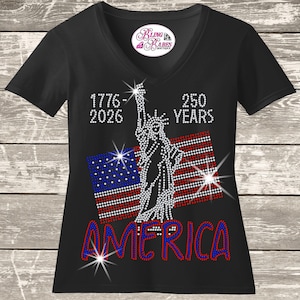 May include: Black V-neck t-shirt with a rhinestone design featuring the Statue of Liberty, American flag, and the word "AMERICA". The design includes the years 1776-2026 and "250 YEARS". A small logo is at the neckline.