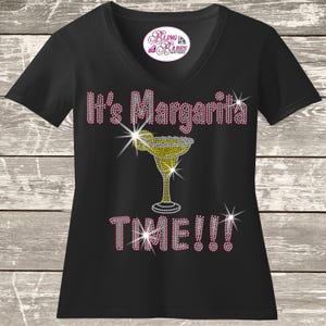 May include: Black V-neck t-shirt with the text "It's Margarita TIME!!!" in pink rhinestones. A margarita glass is in the center, also made of rhinestones. The shirt has a small logo at the neckline.