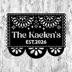May include: A black rectangular decorative panel featuring intricate laser-cut floral patterns along the top and bottom edges. The centre displays the white text The Kaelen's and EST.2026, set against a textured, distressed grey background.