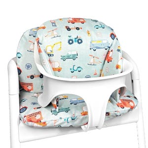 Peut inclure: Une chaise haute blanche dotée d'un coussin de siège rembourré sur fond bleu clair, orné d'un motif coloré de divers véhicules, dont des camions de pompiers, des hélicoptères, des voitures et des scooters. Harnais de sécurité en plastique blanc.