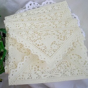 May include: A stack of ivory lace paper envelopes with a delicate floral pattern. The envelopes are folded and ready to be used for special occasions.
