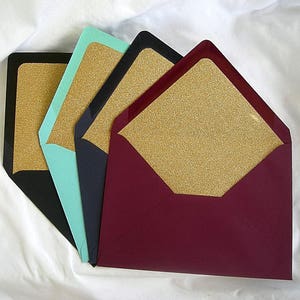 May include: Four envelopes with gold glitter lining. The envelopes are in different colors: teal, black, navy blue, and burgundy.