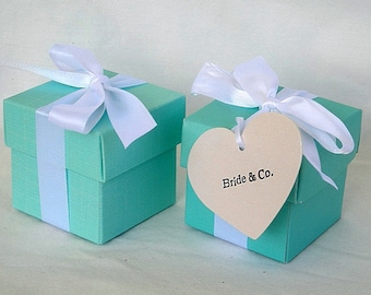 May include: Two teal blue gift boxes with white satin ribbon bows. The box on the right has a heart-shaped tag that says "Bride & Co."