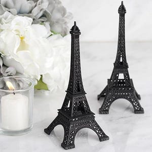 May include: Two black Eiffel Tower figurines on a white surface. The towers are detailed and have a classic design.