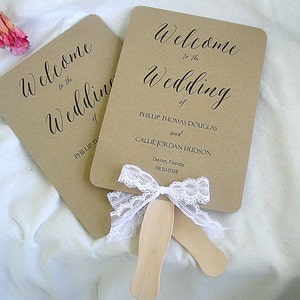 May include: Two brown paper fans with white lace ribbon bows. The fans have the text "Welcome to the Wedding of Phillip Thomas Douglas and Callie Jordan Hudson" and "Destin, Florida 09.10.2016".