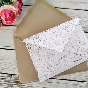 May include: A white doily envelope with a brown envelope underneath. The doily envelope has a delicate lace pattern.