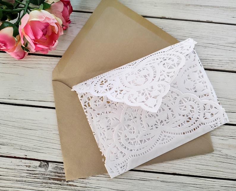 May include: A white doily envelope with a brown envelope underneath. The doily envelope has a delicate lace pattern.