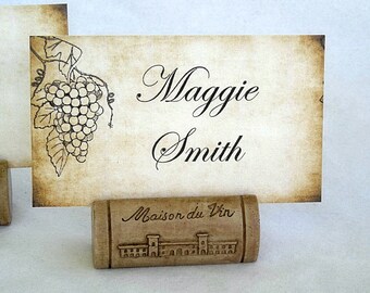 May include: A vintage-style place card with the name "Maggie Smith" printed on it. The card is held by a cork place card holder with the text "Maison du Vin" and a small illustration of a building.