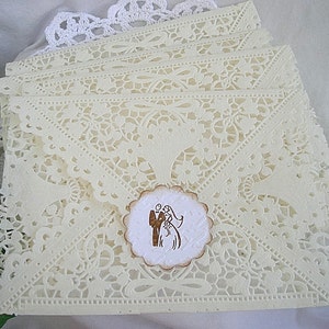 May include: A stack of ivory lace wedding invitations with a brown and white paper circle with a silhouette of a bride and groom.
