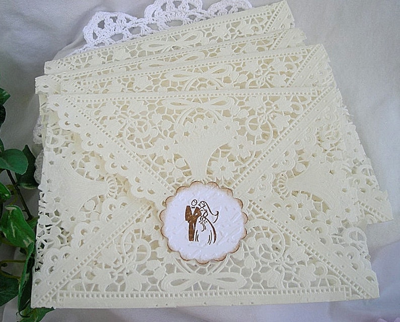 May include: A stack of ivory lace wedding invitations with a brown and white paper circle with a silhouette of a bride and groom.