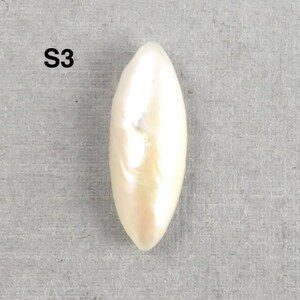 May include: A single, elongated, pearlescent white bead with a subtle, warm hue. The bead has a smooth, polished surface and a slightly irregular shape. The text "S3" is visible in the upper left corner.