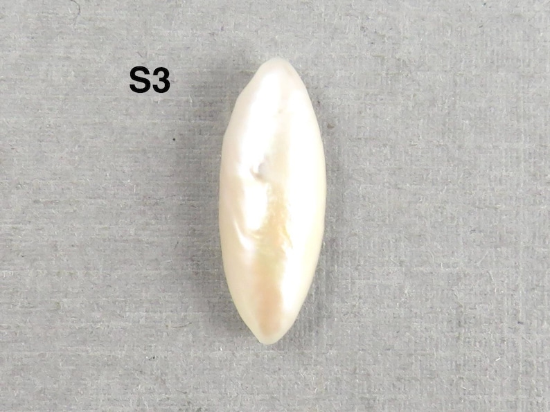 May include: A single, elongated, pearlescent white bead with a subtle, warm hue. The bead has a smooth, polished surface and a slightly irregular shape. The text "S3" is visible in the upper left corner.