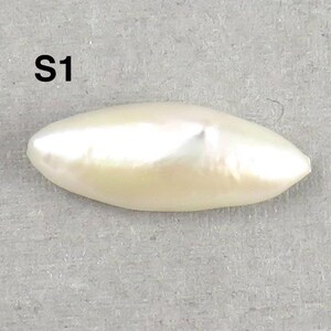 May include: A lustrous, off-white, elongated pearl with a smooth surface. The pearl has a slight luster and a subtle, creamy hue. The text "S1" is printed in black at the top of the image. The pearl is set against a gray background.