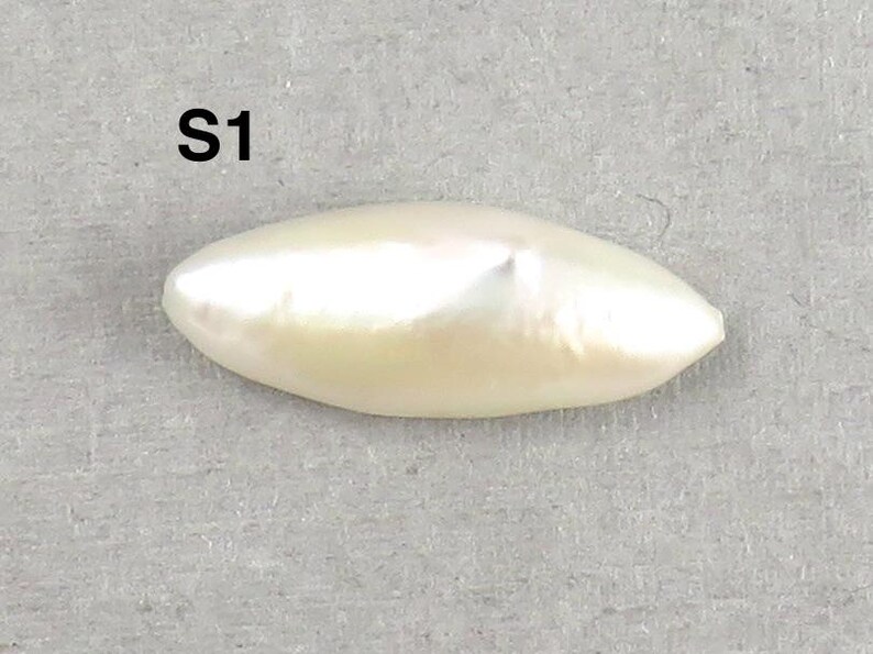 May include: A lustrous, off-white, elongated pearl with a smooth surface. The pearl has a slight luster and a subtle, creamy hue. The text "S1" is printed in black at the top of the image. The pearl is set against a gray background.