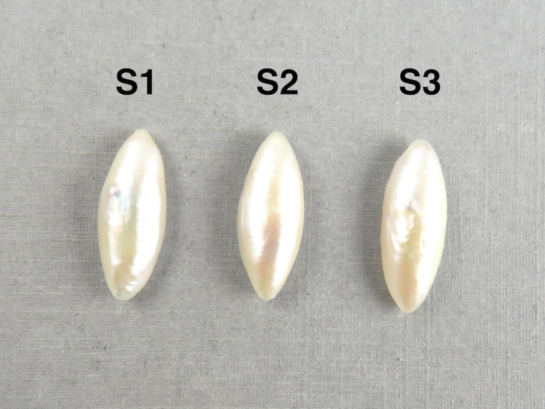 May include: Three elongated, off-white pearls are displayed against a gray background. Each pearl is labeled with a black capital "S" followed by a number. The pearls have a pearlescent sheen, reflecting light.