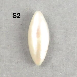 May include: A single, elongated, cream-colored pearl with a smooth, glossy surface. The pearl has a pointed, teardrop shape and is set against a gray background. The text "S2" is in the upper left corner.