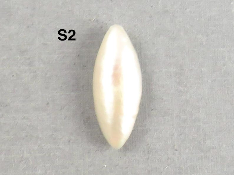 May include: A single, elongated, cream-colored pearl with a smooth, glossy surface. The pearl has a pointed, teardrop shape and is set against a gray background. The text "S2" is in the upper left corner.