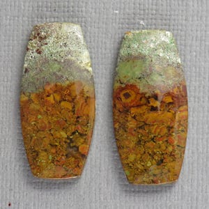 May include: Two elongated, rectangular cabochons with rounded corners, featuring a polished surface. The stones display a distinct color gradient, transitioning from a textured, earthy mustard yellow and burnt orange base to a pale, mottled mint green top.