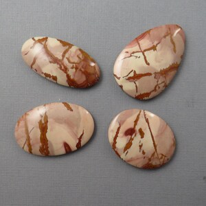 May include: Four polished, oval-shaped stones with a cream and reddish-brown pattern. The stones vary slightly in shape and size, with the largest measuring approximately 2 inches in length. The natural patterns create a unique appearance.