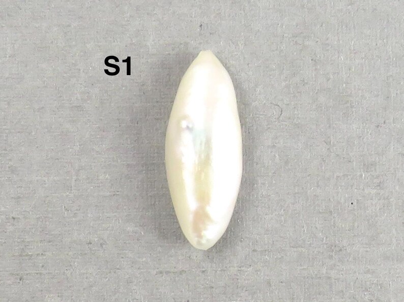 May include: A lustrous, elongated, white pearl with a subtle iridescent sheen. The pearl has a smooth, oval shape and is set against a neutral gray background. The text "S1" is visible in the upper left corner.
