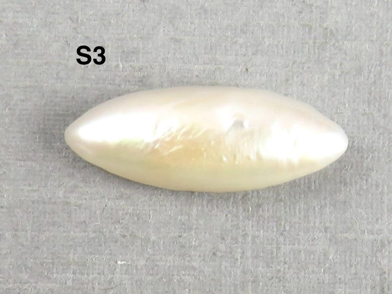 May include: A lustrous, off-white, elongated pearl with a smooth surface. The pearl has a subtle, iridescent sheen and a slightly irregular shape. The text "S3" is visible in the upper left corner.