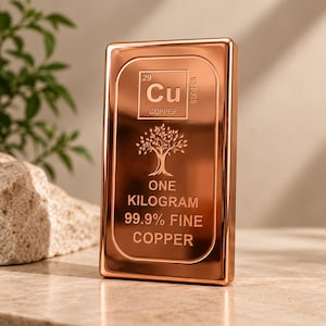 May include: A rectangular copper bar with a polished finish. The front features the periodic table symbol Cu, the atomic number 29, a tree graphic, and the text: ONE KILOGRAM 99.9% FINE COPPER. The bar has a smooth, reflective surface and rounded edges.