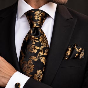 May include: A black necktie and matching pocket square featuring a gold floral pattern, worn with a white dress shirt, a black suit jacket, and black and gold circular cufflinks. The set displays a consistent metallic gold botanical design.