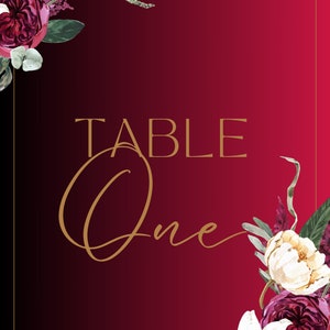 May include: A burgundy table number card with gold text that reads "TABLE One." The card is decorated with watercolor floral arrangements in shades of white, burgundy, and green, with a gold border.