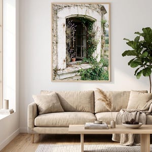 May include: A framed wall art print featuring a stone window frame overgrown with green ivy and purple lavender flowers. The image shows a rustic, weathered stone structure with a dark wooden window frame, capturing a natural, outdoor scene.
