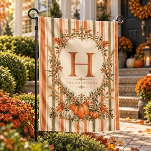 Peut inclure: Un drapeau de jardin rectangulaire à rayures verticales orange et crème. Le centre présente une grande lettre H orange dans une couronne ovale de feuilles d'automne, de glands et de blé. Sous la lettre, le texte indique THE HARRISONS avec des citrouilles.