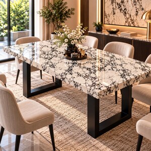 May include: A rectangular dining table with a white and black speckled stone top and a thick black metal U-shaped base. The table is surrounded by six beige upholstered chairs with dark legs, and a vase of white flowers sits in the centre.