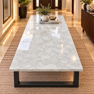 Puede incluir: Una mesa de centro rectangular con un tablero de piedra estilo terrazo en tonos blancos y grises con acabado pulido. La mesa se apoya sobre una estructura de metal negro resistente con una base en forma de U que aporta estabilidad.