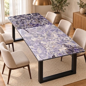 May include: A rectangular dining table featuring a polished purple amethyst gemstone surface with a faceted, crystalline texture. The table is supported by a sturdy black metal frame with two U-shaped legs and is surrounded by four beige upholstered chairs.
