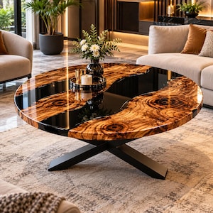 May include: A round coffee table featuring a natural wood slab with prominent swirling grain patterns and a glossy finish, bisected by a smooth, opaque black resin river. The table is supported by a black metal base with an X-shaped design.