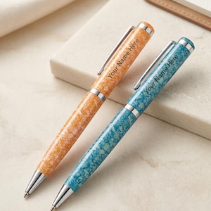 May include: Two ballpoint pens with a marbled finish, one in orange and one in blue. Each pen features a silver clip, a silver tip, and the text Your Name Here printed on the barrel. The pens have a glossy, textured appearance with metallic accents.