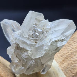 Peut inclure: Un amas de cristaux minéraux translucides et incolores aux bords tranchants et anguleux, formant une structure géométrique. L'ensemble présente de multiples pointes rayonnant depuis un cœur central, avec des facettes nettes et une surface vitreuse.