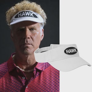 May include: A white visor featuring a black oval patch on the front brim with the word HAWK embroidered in white capital letters. The visor has a structured brim and an adjustable strap at the back, designed for sun protection and athletic wear.