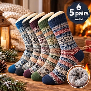 Puede incluir: Cinco pares de calcetines con un patrón geométrico de inspiración nórdica que incluye copos de nieve y rayas. Cada calcetín tiene la puntera y el talón de un color sólido. Un recuadro circular muestra el forro de felpa grueso y gris claro.