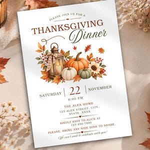 May include: A white Thanksgiving dinner invitation card featuring a central illustration of a lantern, pumpkins, sunflowers, and autumn leaves. The text includes the date Saturday, November 22 at 6:00 PM, location details, and RSVP information.