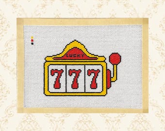 May include: A needlepoint canvas featuring a yellow slot machine design with the word LUCKY in red text above three white reels displaying the number 777 in red. A red lever is attached to the right side, and a small color key is visible on the left.
