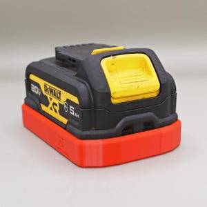 以下が含まれることがあります： 上部に黄色いリリースボタンを備えた黒と黄色のDeWalt 20V XR 5Ah電動工具用バッテリーパック。側面には小さなロゴが印刷された、明るいオレンジ色の長方形のプラスチック製ベースマウントに固定されています。