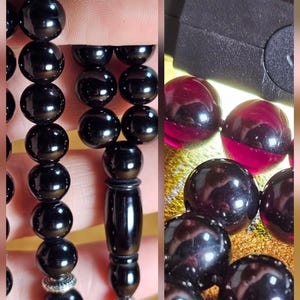 May include: A string of polished black spherical beads featuring a central elongated bead and silver-toned metal accents. The beads appear translucent and deep red when held against a bright light source, showing a smooth, reflective surface finish.
